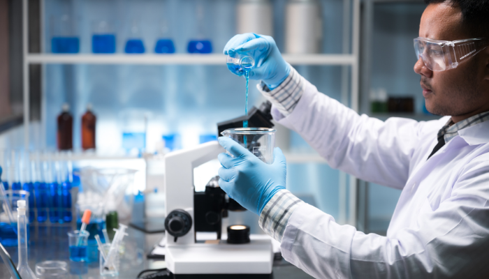 Scientist pouring blue liquid into a beaker in a laboratory