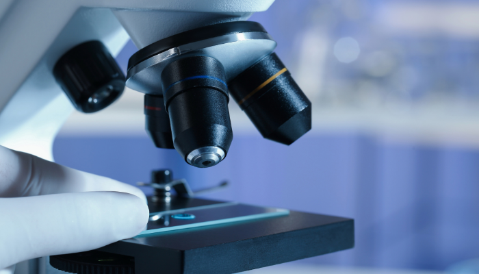 En hand i handske placerar ett objektglas under ett laboratoriemikroskop